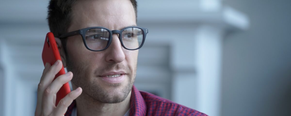 Thoughtful young German businessman in glasses having urgent conversation on mobile phone