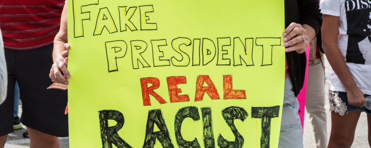 Women protesting with sign that says fake president real racist